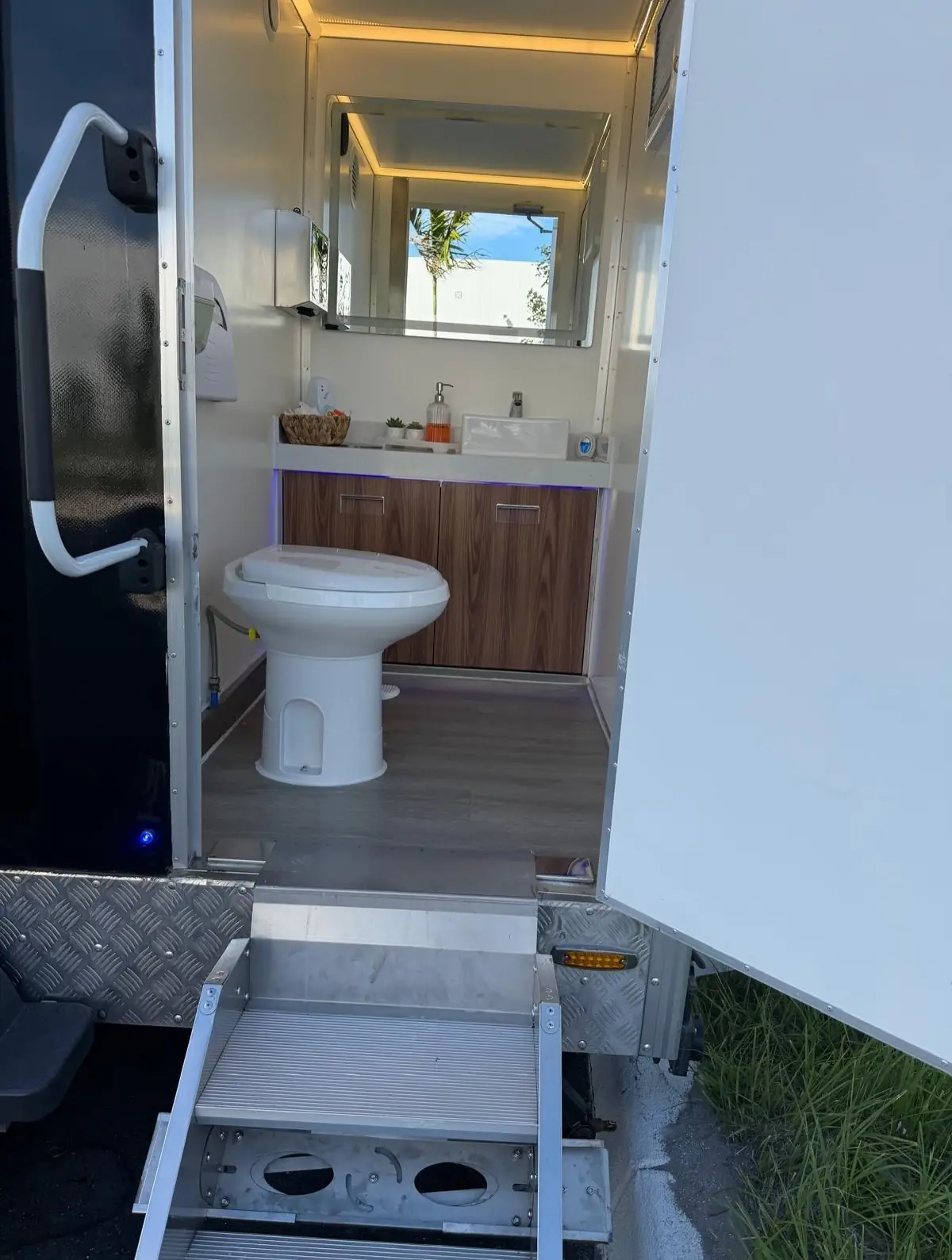 Restroom trailer interior with a toilet, wood vanity and lighted mirror