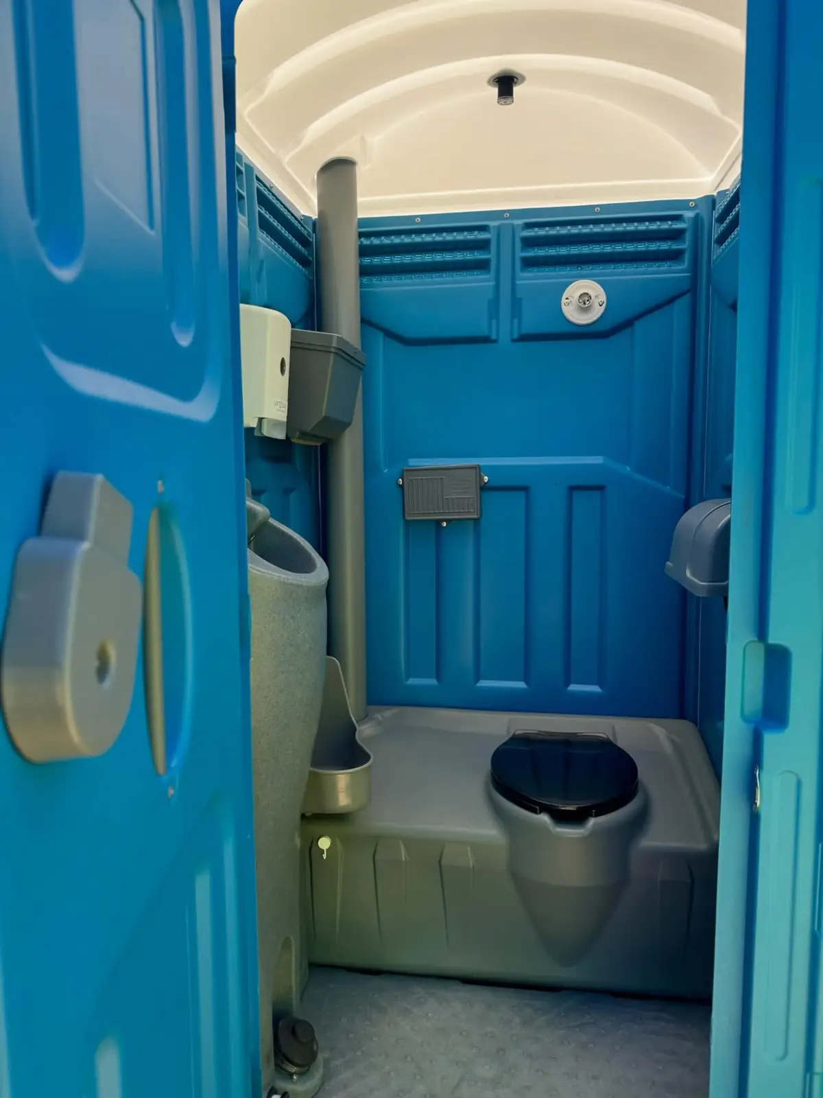 Inside a blue standard porta potty showing the toilet seat, urinal and vent