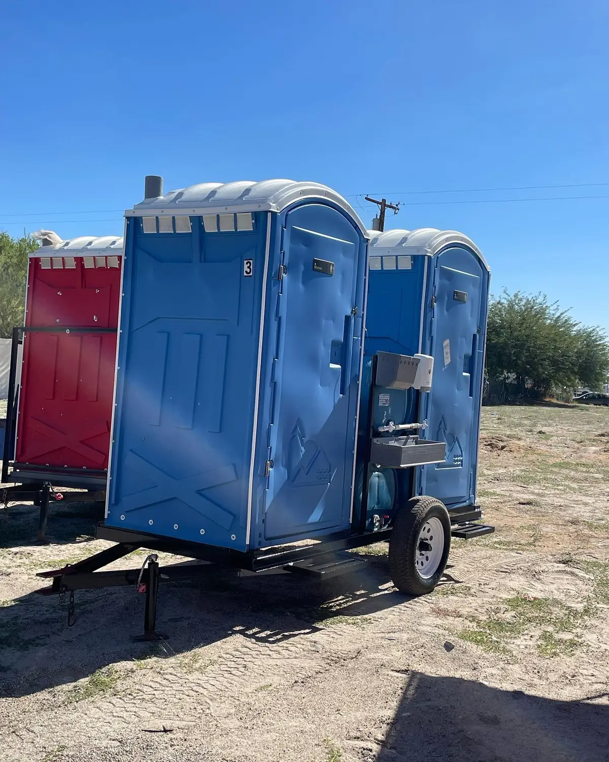 Blue portable toilet strapped to a towable trailer on open ground